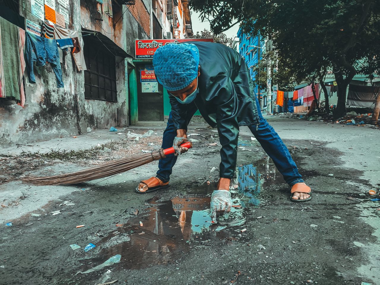 A person wearing a mask and gloves cleaning the street in a Bangladesh neighborhood.