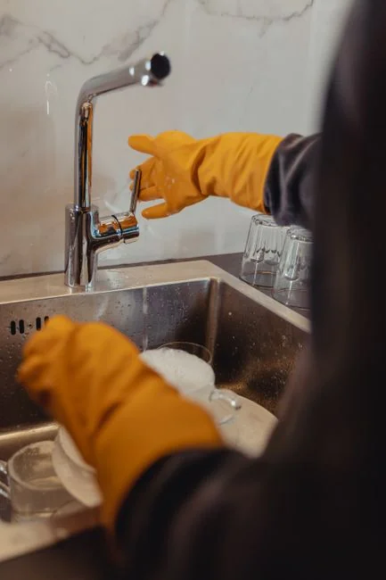 A pair of hands is using a green scrub pad to wash a white plate indoors.